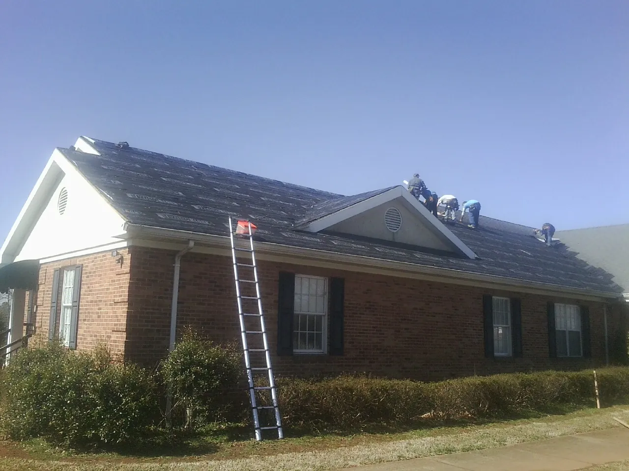Crew tearing shingles off a brick ranch roof with a ladder set — Emergency Roof Repair work by our crew in Danville